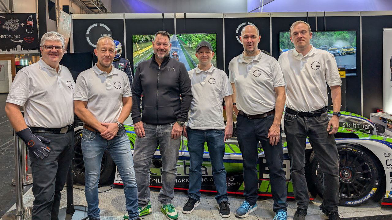 The GCOM360 team in front of the LMP3 race car at the SimRacing Expo 2025 booth